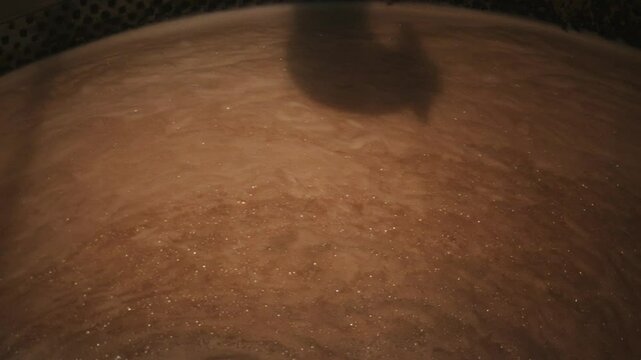 Wort, a sugary liquid extracted from malted grains, is mixing in a large stainless steel tank at a brewery, marking a crucial stage in the beer production process