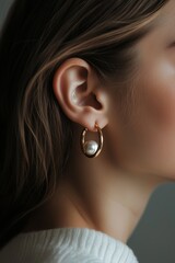 Elegant woman showcasing gold hoop earrings with pearl detail in a simple, neutral background during a serene indoor setting