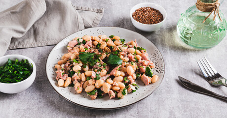 Appetizing salad with tuna, white beans and greens on a plate on the table web banner