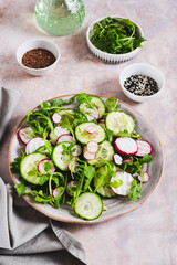 Cucumber, radish and greens salad mix on a plate on the table vertical view