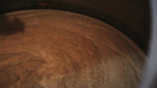 Wort, a sugary liquid extracted from malted grains, is mixing in a large stainless steel tank during the beer brewing process, showing the swirling motion and creating a mesmerizing visual