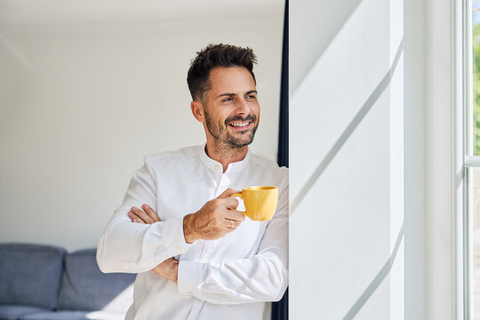 Portrait of adult man drinking coffee at home looking out the window