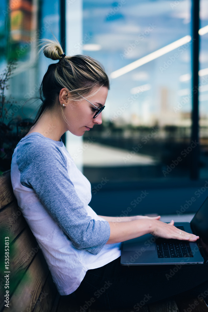 Fototapete pensive female student keyboarding on netbook searching tutorial while sitting outdoors on bench,hip