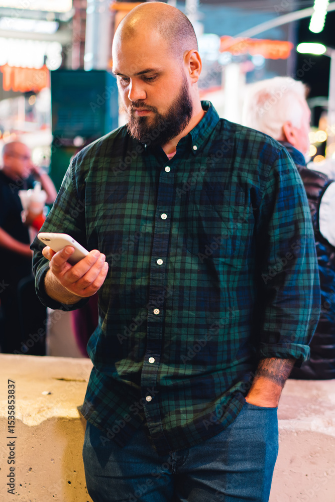 Poster pensive bearded man holding mobile phone reading message standing on times square at evening,hipster