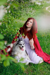red-haired girl with curly hair sits with a marble-colored border collie dog. The girl in the...