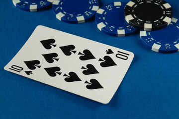 Close-up of a ten of spades playing card resting on a blue surface surrounded by various colorful poker chips, creating an energetic atmosphere for a card game