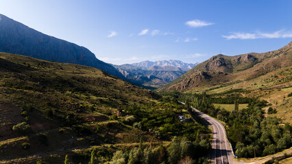 A winding road between mountains captured by drone. Stunning nature with hills, steppe and forest.