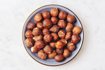Small portion of hazelnuts. Blue ceramic plate on white marble table. Healthy snack idea. Minimalistic top view. Tapas style nuts. Vegetarian protein source. Simple elegant presentation.