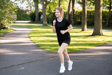 Teenager running on a sunny morning in a park, wearing athletic gear, showcasing determination and...