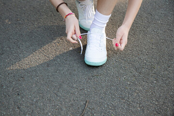 Individual is tying shoelaces on athletic sneakers while preparing for outdoor sports activity on a...
