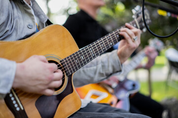 close up of acoustic guitar player performing live music outdoors with band, fingers strumming...