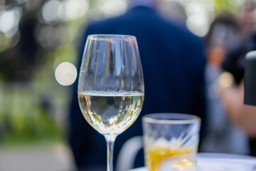 close up of white wine glass and cocktail on table at elegant outdoor event or wedding reception with guests in background, celebratory atmosphere with drinks, social gathering, summer party scene
