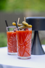 two bloody mary cocktails in crystal glasses with pickles and olives on skewers, served on white...