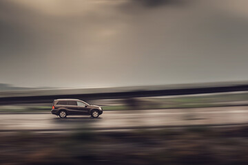 Brown SUV driving down the street in rainy weather. Speed blurred background, side view