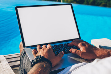Cropped image of male hands typing text information on keyboard of modern laptop computer with blank copy space screen for your advertising content during remote work in summertime near pool