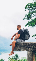 Bearded male hiker with backpack admiring nature of green high mountains during summer trip in asia...
