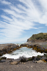 Rocky shoreline with waves and distant cliffs under a blue sky
