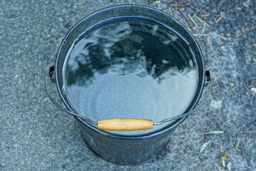 top one industrial black iron new traditional with handle with clean transparent water round garden bucket stands on asphalt daytime outdoors