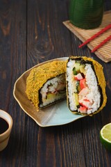 Fried sushi burgers in breading with crab sticks, cucumber and avocado filling on leaf-shaped plate on dark wooden background. Asian cuisine.