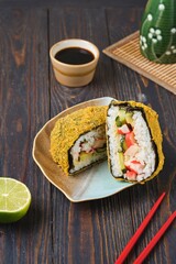 Fried sushi burgers in breading with crab sticks, cucumber and avocado filling on leaf-shaped plate on dark wooden background. Asian cuisine.