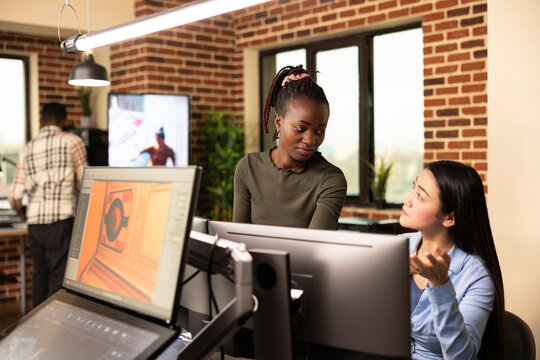 Professional women editors exchanging ideas, collaborating on a startup design project in brick wall office. Asian female employee sitting at desk and updating her black creative manager.