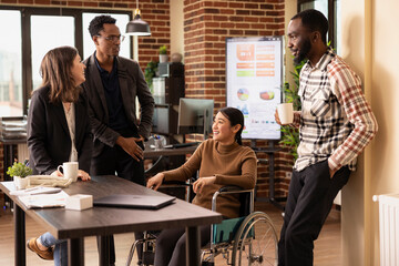 Multiethnic colleagues gather around a desk, taking a break and sharing stories in a relaxed office...