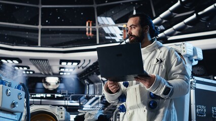 Astronaut reviewing onboard analytics on laptop before stepping out for scheduled operations...