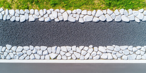 Aerial view of a gravel path bordered by white rocks with a strip of grass on one side and pavement on the other. Contrast and texture in landscape design