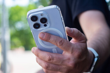 Close-up of a man hand holding a white smartphone in a transparent case. Technological lifestyle in an urban environment.