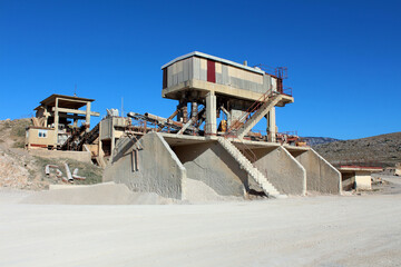 A large concrete quarry processing plant with conveyor belts, storage bins, and metal stairs stands...