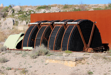 Large black biofilter wheels with metal frames are arranged in a row at an outdoor industrial site,...