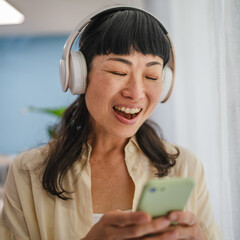 Playful japanese woman listen music on headphones and hold cellphone