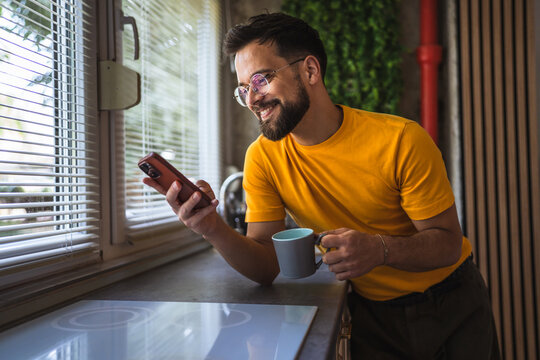 cheerful adult man drink coffee and use mobile phone in the kitchen