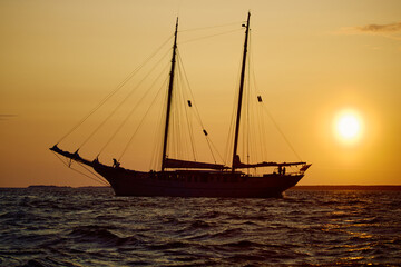 The silhouette of an ancient frigate in the sea at sunset, splashes of waves illuminated by the sun