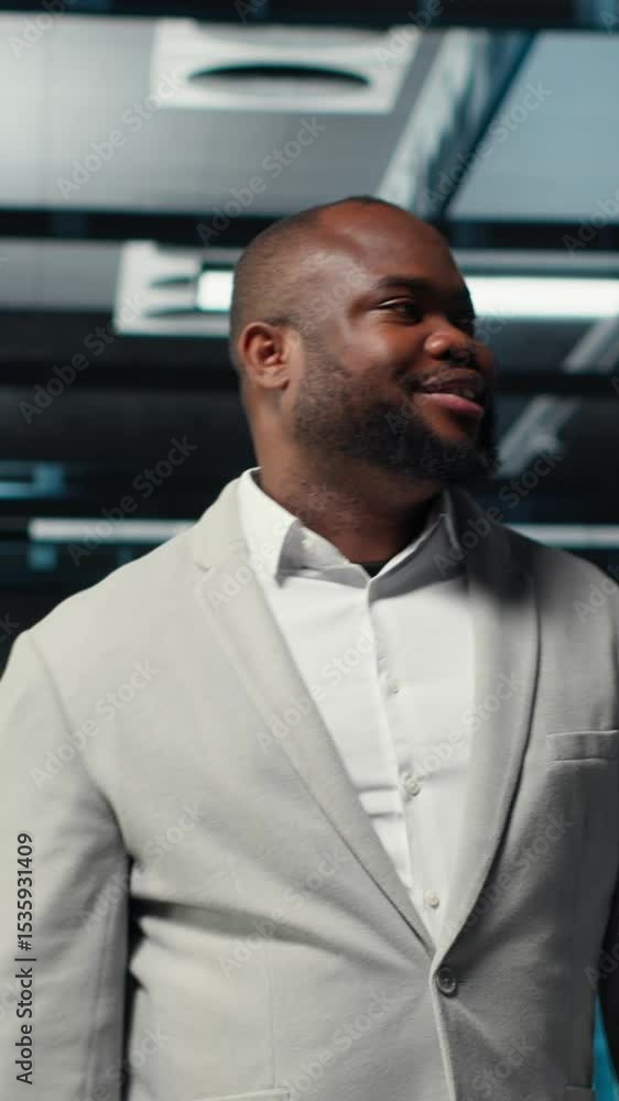 Poster vertical video smiling engineer walking in data center, checking hardware for system stability. happ