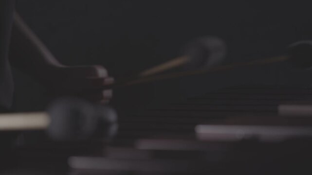 A close-up, low-angle shot of a musician passionately playing a marimba or vibraphone with mallets in a dark, atmospheric setting. Ungraded LOG footage for color grading.