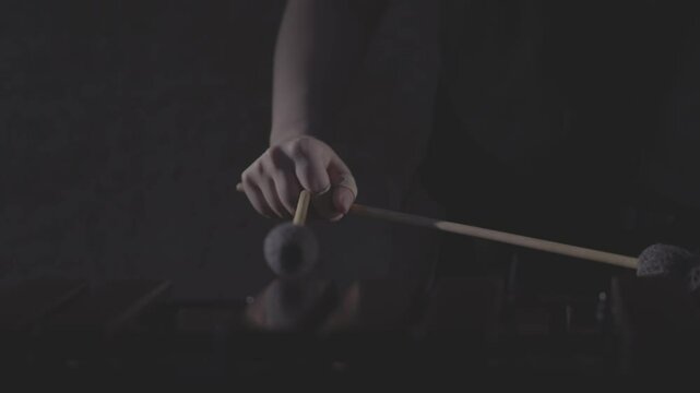 A close-up, low-angle shot of a musician passionately playing a marimba or vibraphone with mallets in a dark, atmospheric setting. Ungraded LOG footage for color grading.
