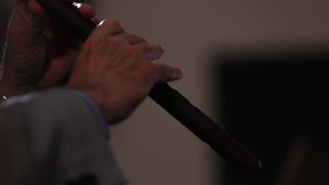 Close-up, handheld footage of a musician's hands playing a traditional ethnic woodwind instrument,  Passionate performance by a man in a formal suit.