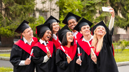 Happy graduates international group of students taking selfie together at university campus, using...