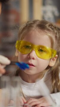 Asian man teacher and wondered little girl in protective glasses look at blue litmus test sitting at table during fun science lesson in classroom closeup