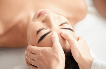 Young attractive korean woman getting acupressure head massage treatment in spa salon. Professional therapist massaging face of beautiful asian female, closeup shot with selective focus