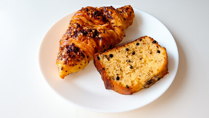 Delicious close-up of a croissant with chopped nuts and a slice of chocolate chip banana bread on a white plate. Perfect for bakery promotions, breakfast menu designs, or food blog visuals.
