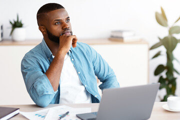 Black Freelancer Guy Sitting At Workplace With Thoughtful Face Expression, Pensive African American...
