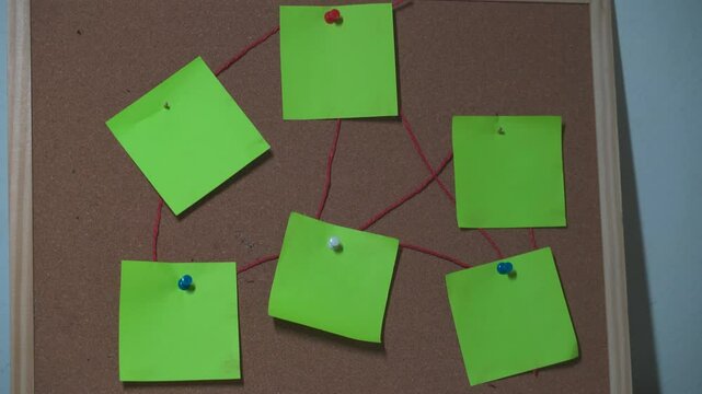 board with  Green sticky notes connected with red thread on pink cork board for brainstorming and planning