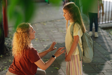 Caring mother kneeling and talking to her elementary school daughter after school