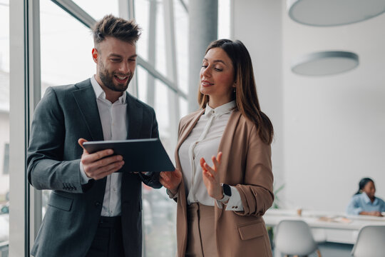 Business colleagues using digital tablet, discussing work in modern office