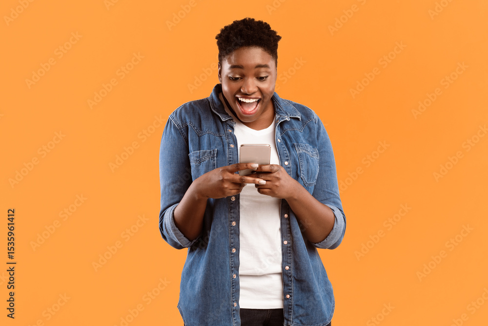 Poster Excited African American Lady Using Cellphone Texting In Social Media Or Playing Mobile Game Standing Over Yellow Studio Background. Great Mobile Application For Your Smartphone Concept