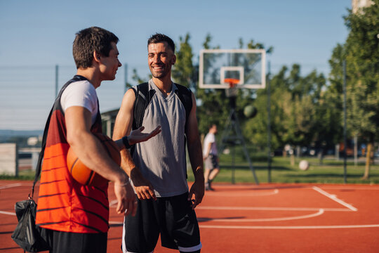 Two male basketball players talking on outdoor court after training