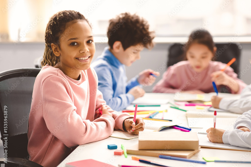 Poster academic concept. smiling junior african american school girl sitting at desk in classroom, writing 