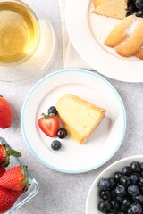 Tasty bundt cake with powdered sugar, berries and tea on light grey table, flat lay